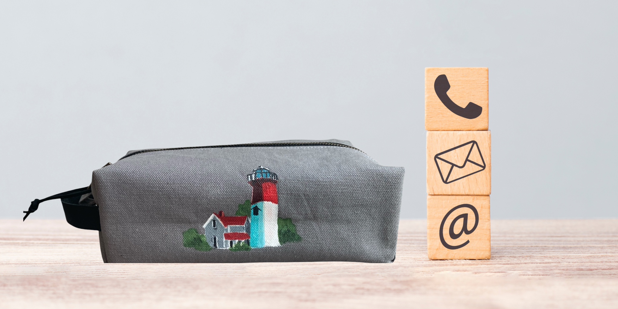 Gray pouch with lighthouse design next to wooden blocks with icons on a light blue background